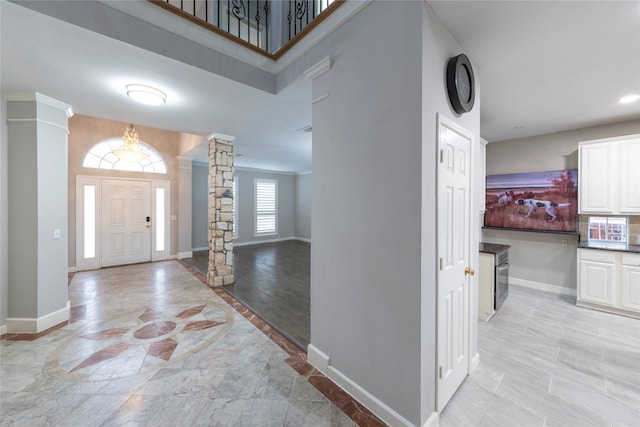 foyer with light wood finished floors, decorative columns, and baseboards