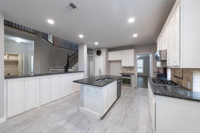 kitchen with stainless steel appliances, a sink, visible vents, white cabinets, and wall chimney range hood