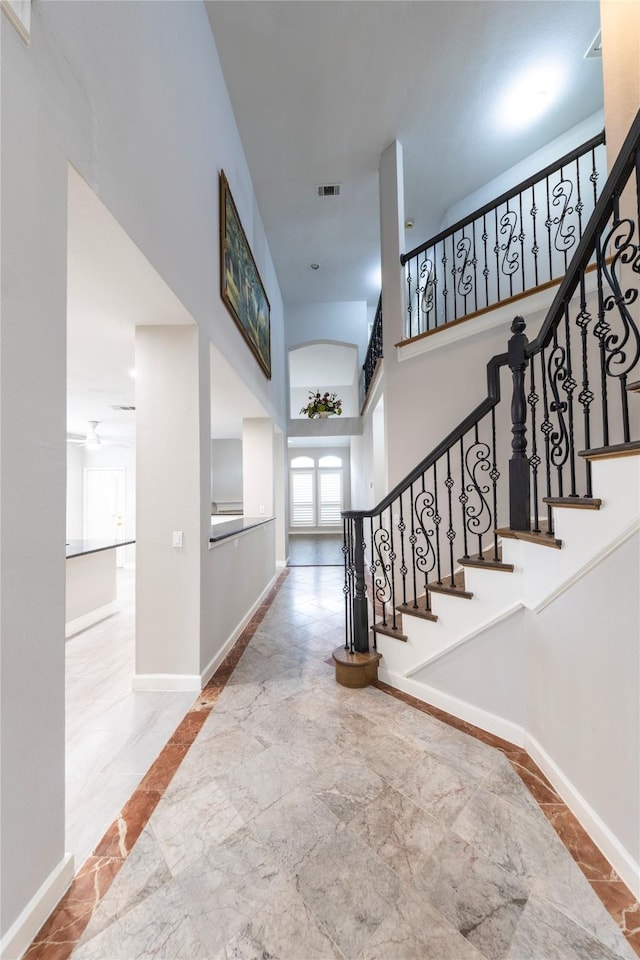 stairway featuring marble finish floor, visible vents, a towering ceiling, and baseboards