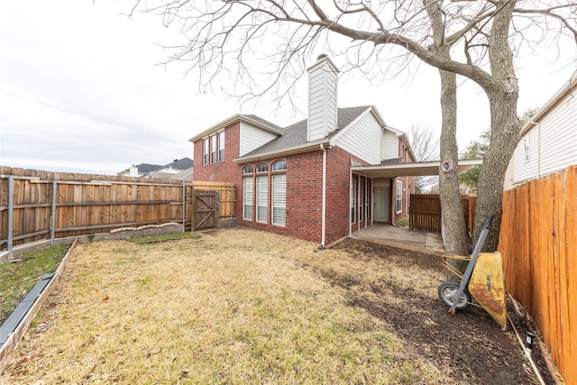 back of house with brick siding, a yard, a chimney, a patio area, and a fenced backyard