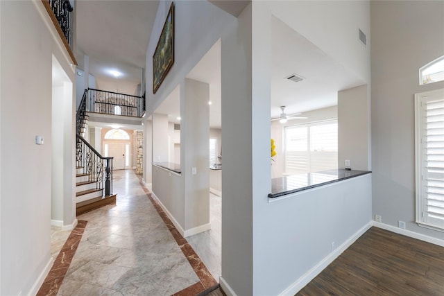 hallway with stairs, a high ceiling, visible vents, and baseboards