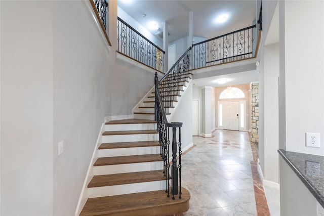 stairs featuring baseboards, decorative columns, and a high ceiling