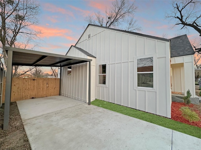 exterior space featuring fence, concrete driveway, roof with shingles, a carport, and board and batten siding