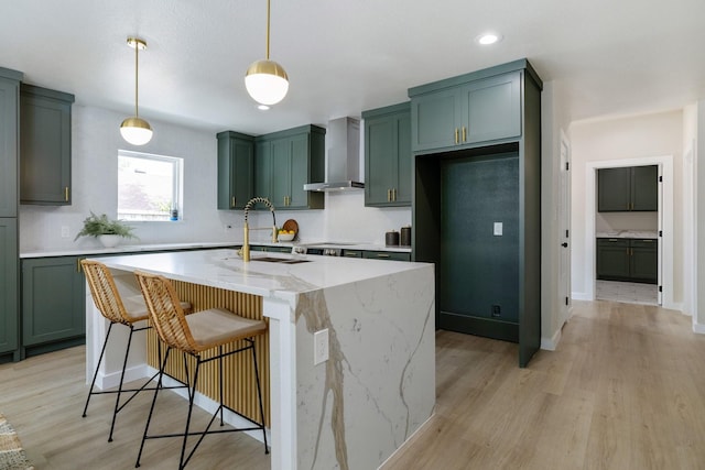 kitchen with green cabinets, wall chimney exhaust hood, a sink, and light stone countertops