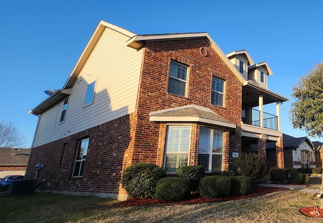 view of home's exterior with brick siding, a yard, and a balcony