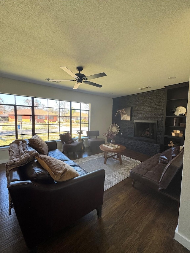 living area featuring built in features, a brick fireplace, ceiling fan, a textured ceiling, and wood finished floors