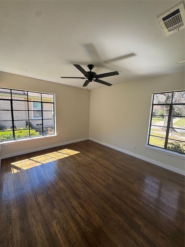 unfurnished room featuring dark wood-style floors, baseboards, visible vents, and a ceiling fan