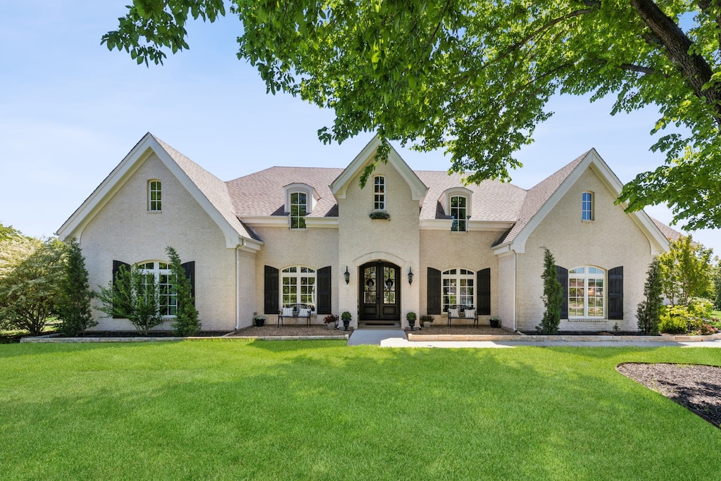 french country inspired facade with brick siding, a front yard, and french doors