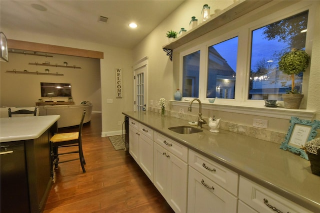 kitchen featuring dark wood-style flooring, visible vents, white cabinets, a sink, and baseboards