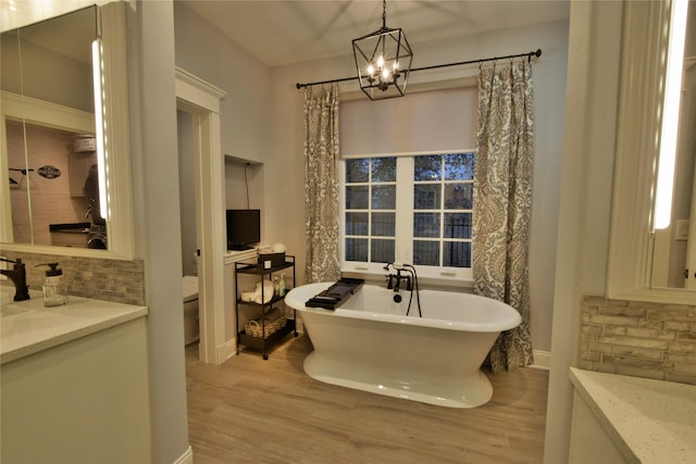 bathroom with a freestanding tub, wood finished floors, vanity, baseboards, and backsplash