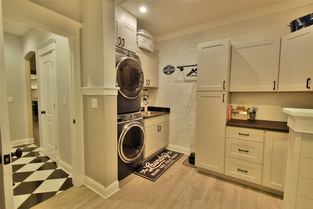 laundry room with arched walkways, stacked washer / dryer, a sink, cabinet space, and light floors