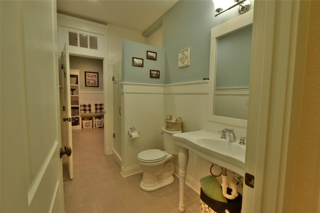 full bath with a wainscoted wall, a stall shower, tile patterned flooring, and toilet