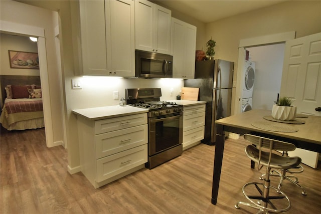 kitchen with stainless steel appliances, stacked washing maching and dryer, light countertops, and light wood-style floors