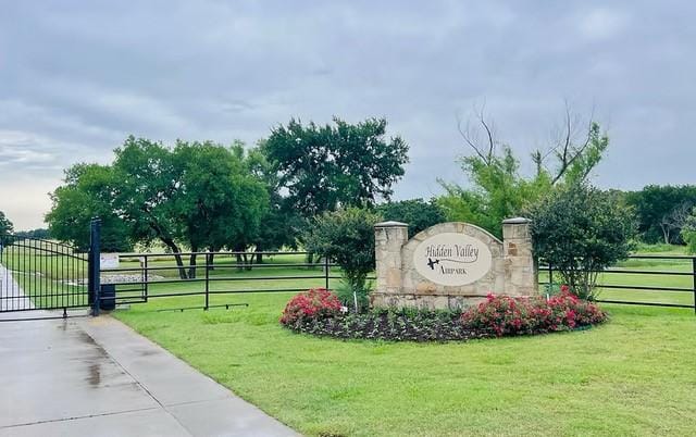 community sign featuring a lawn, fence, and a gate