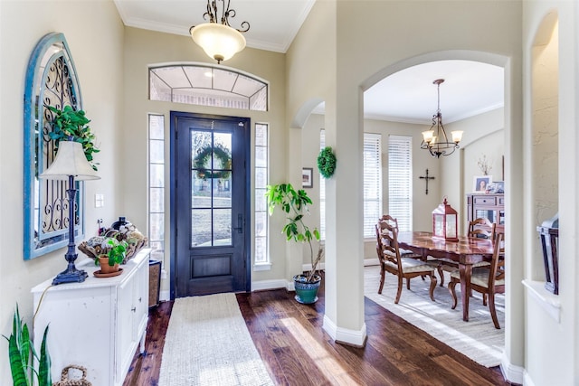 foyer entrance with arched walkways, dark wood-style flooring, a notable chandelier, ornamental molding, and baseboards