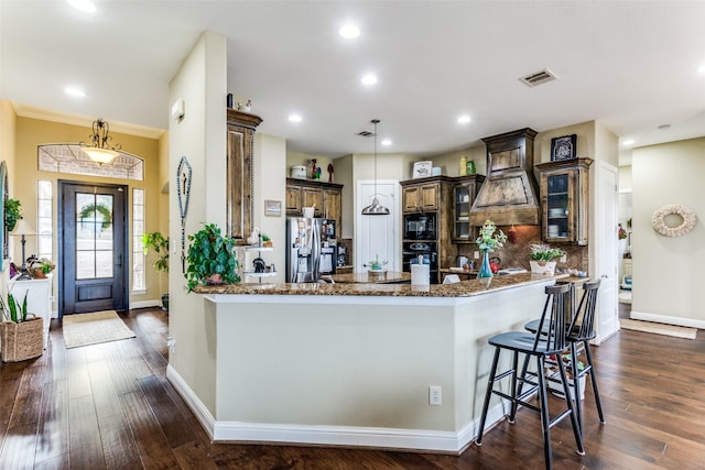 kitchen with black microwave, a peninsula, backsplash, dark stone countertops, and stainless steel fridge