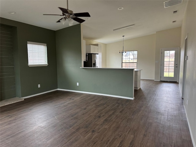 unfurnished living room featuring ceiling fan with notable chandelier, dark wood-style flooring, visible vents, baseboards, and vaulted ceiling