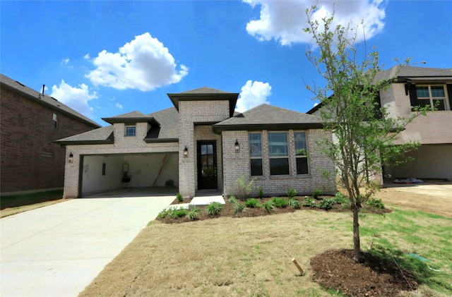 prairie-style house with a garage, brick siding, concrete driveway, roof with shingles, and a front yard