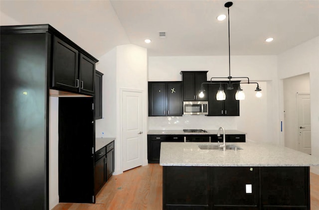 kitchen featuring appliances with stainless steel finishes, light wood-type flooring, dark cabinetry, and a sink