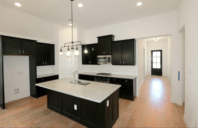 kitchen with stainless steel appliances, light wood-type flooring, dark cabinetry, and a sink