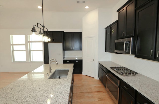 kitchen with appliances with stainless steel finishes, dark cabinetry, a sink, and light stone counters