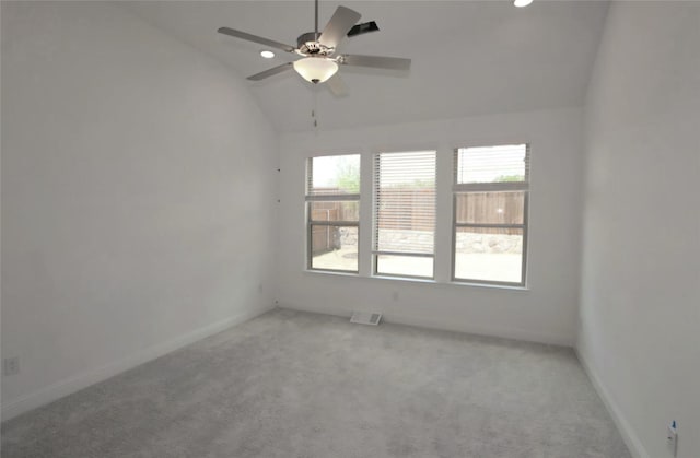 spare room with light colored carpet, visible vents, a ceiling fan, vaulted ceiling, and baseboards