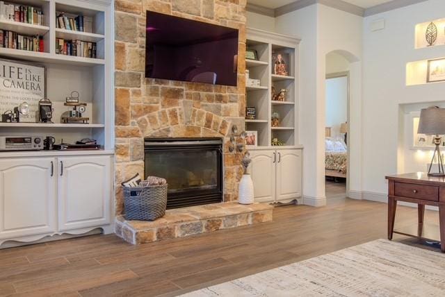 living room with arched walkways, light wood finished floors, ornamental molding, a stone fireplace, and baseboards