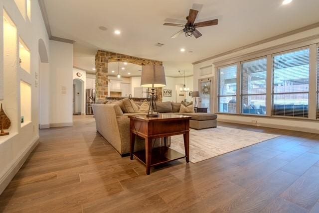 living room featuring arched walkways, ceiling fan, recessed lighting, light wood finished floors, and crown molding