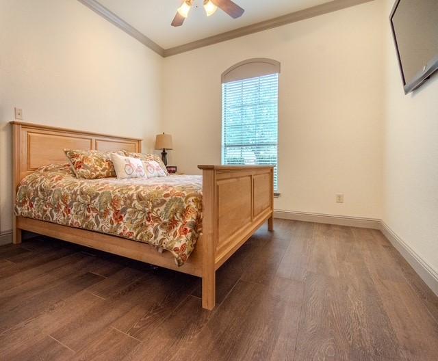 bedroom featuring a ceiling fan, crown molding, baseboards, and dark wood-style flooring