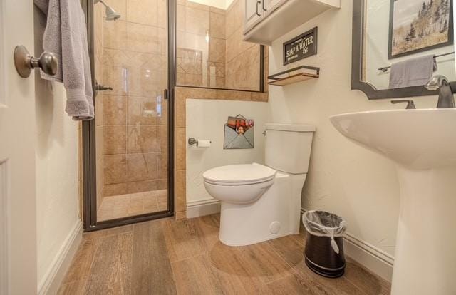 full bath featuring wood finished floors, a shower stall, toilet, and baseboards