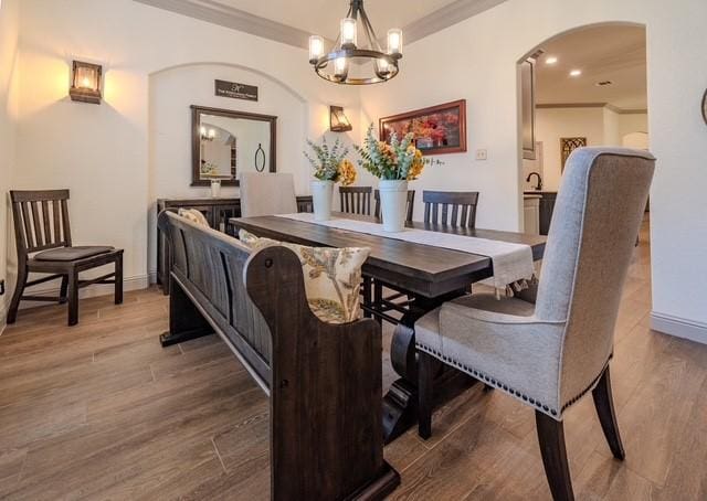 dining room featuring arched walkways, wood finished floors, baseboards, ornamental molding, and an inviting chandelier