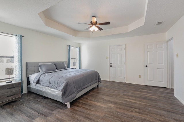 bedroom with dark wood-style floors, a tray ceiling, visible vents, and baseboards