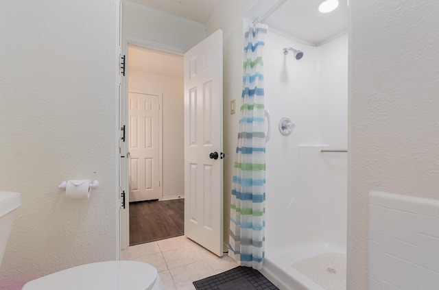 full bathroom with toilet, a stall shower, a textured wall, and tile patterned floors