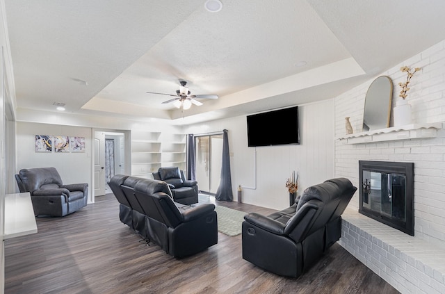 living area featuring a textured ceiling, built in shelves, a fireplace, wood finished floors, and a raised ceiling