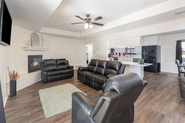 living room featuring a tray ceiling, a fireplace, dark wood finished floors, and visible vents