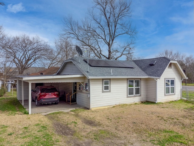 rear view of house with roof with shingles, roof mounted solar panels, and a yard