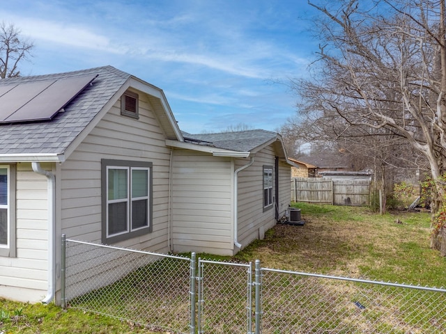 view of side of home with roof with shingles, a yard, roof mounted solar panels, a gate, and fence private yard