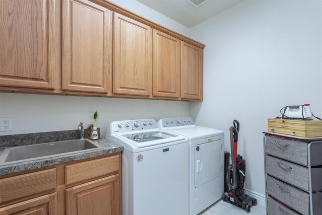 laundry area featuring washing machine and dryer, cabinet space, a sink, and baseboards