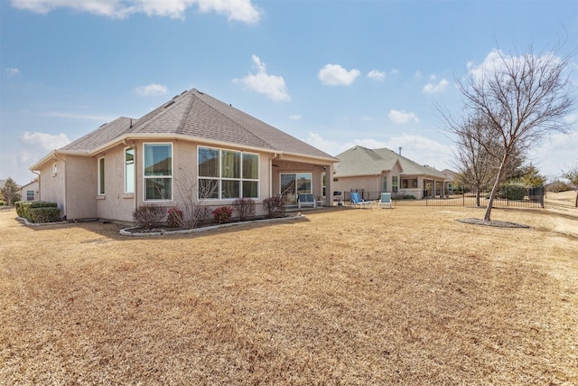 rear view of house with a patio, stucco siding, a shingled roof, a lawn, and fence