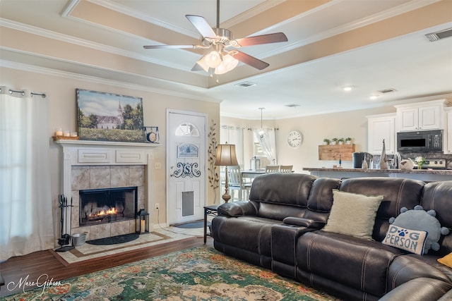 living area featuring a tiled fireplace, visible vents, and wood finished floors