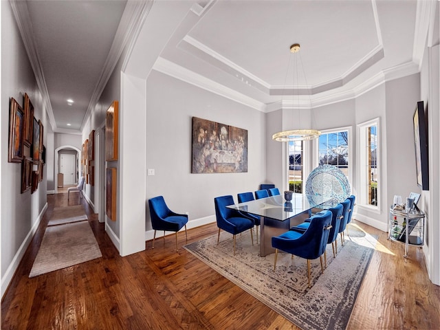 dining space with arched walkways, wood finished floors, a raised ceiling, and crown molding