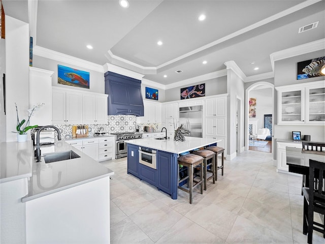 kitchen with premium appliances, blue cabinets, a sink, white cabinetry, and custom range hood