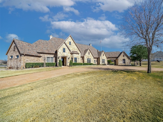 french country inspired facade with stone siding, a chimney, and a front yard