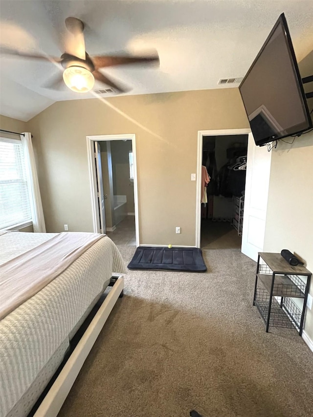 carpeted bedroom featuring lofted ceiling, connected bathroom, a ceiling fan, visible vents, and a walk in closet