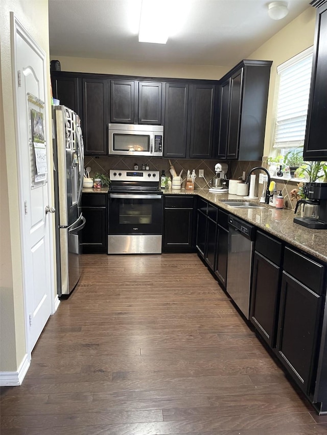 kitchen featuring dark wood-style flooring, stainless steel appliances, backsplash, stone countertops, and a sink