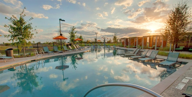 pool at dusk with a patio area, fence, and a community pool