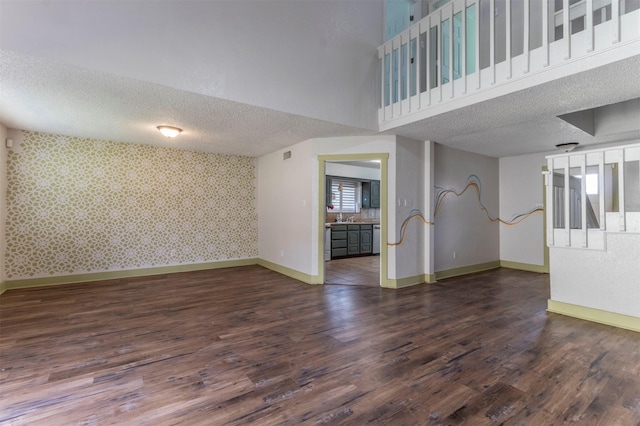 unfurnished living room featuring wallpapered walls, baseboards, wood finished floors, a textured ceiling, and a sink