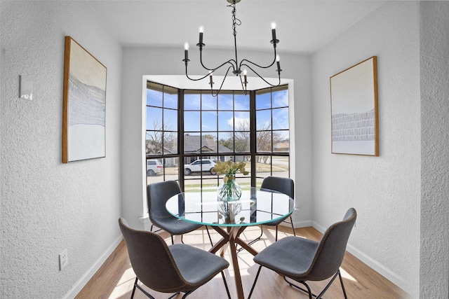 dining space with an inviting chandelier, baseboards, wood finished floors, and a textured wall