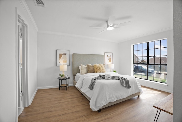 bedroom with baseboards, visible vents, ceiling fan, ornamental molding, and wood finished floors