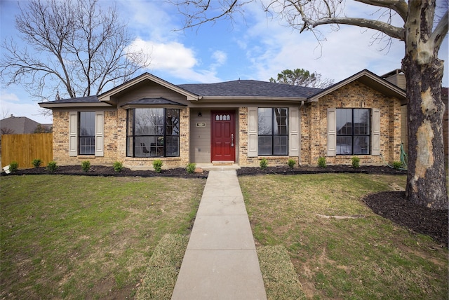 view of front of house with a shingled roof, fence, a front lawn, and brick siding